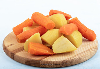Boiled carrots and potatoes for salad on a wooden cutting board.