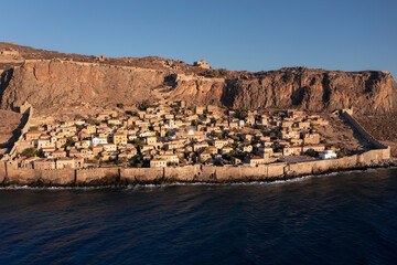 Aerial view of ancient city Monemvasia behind fortress wall on shore of island at sunrise, Greece