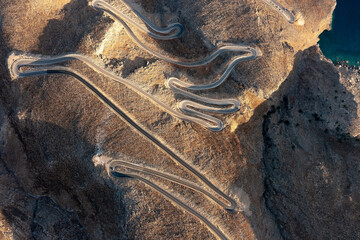 Top-down aerial view of a winding road in desert hills near the coastline at sunset, Crete, Greece - obrazy, fototapety, plakaty
