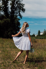 A girl in a rustic dress turned her back and holds flowers in her hand