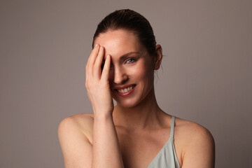 Fototapeta premium Smiling and optimistic woman with glowing skin and natural makeup at studio. 