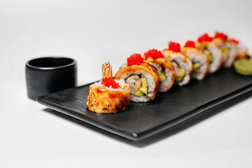 Sushi, rolls. Chinese and Asian cuisine, sets of rolls of ginger and soy sauce lie on a black board with chopsticks. Sushi is made in sets