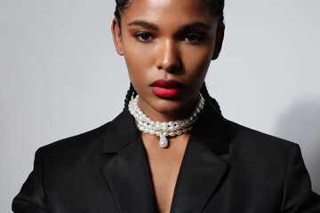 Cropped portrait of African young woman with long braids wears pearl necklaces.