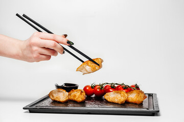 Female hand takes tereyaki from a black plate on a white background. Chinese and Asian cuisine