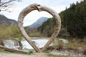 Wooden heart in nature - Heart made of wood in front of a waterfall and a forest. Valentine's Day and romantic nature concept. 