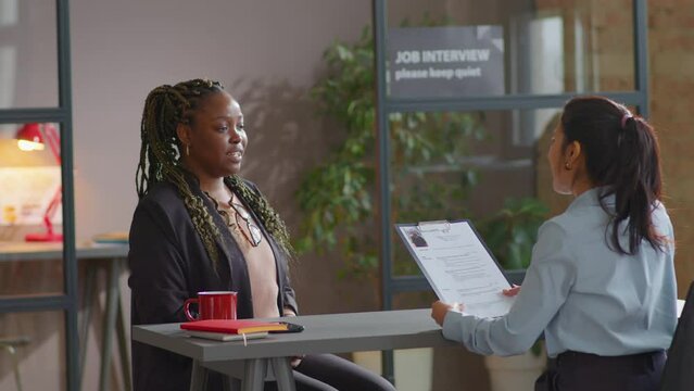 Young African American female candidate giving CV to HR manager and answering questions during job interview in office