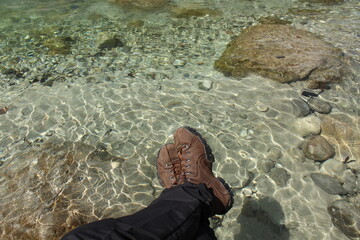 Hiking shoe boots - resting at a river with transparent water, sand and stones 