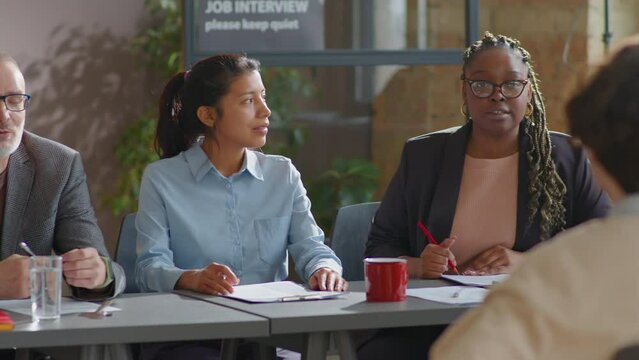 Committee of multiethnic male and female recruiters speaking with candidate during job interview in office