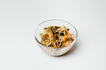 Asian salad with seaweed and carrots in a transparent plate on a white background