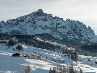 View of the Reddish Rocks of the Snow-covered italian Dolomites with Fir Trees and typical Mountain Dwellings