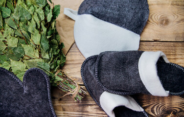 A dry birch broom and soft slippers lie on a wooden background. Accessories for baths and saunas.