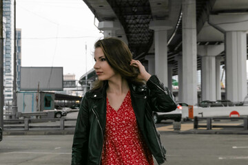 Fototapeta na wymiar a girl in glasses, a black leather jacket and a red dress is standing under the overpass