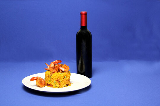 Traditional paella rice from Valencia Spain, made with saffron shellfish, shrimp and vegetables served on a white plate accompanied by red wine on a blue background	