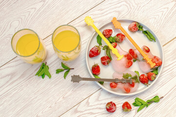 Frozen ice with red strawberry, mint in guitar shape for cold fresh summer lemonade cocktail drinks with orange juice. Homemade sweet fruit berry ice cream popsicles dessert food on gray plate