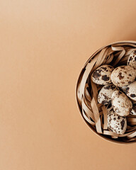 Quail eggs in a round wooden box on a beige background. Top view.
