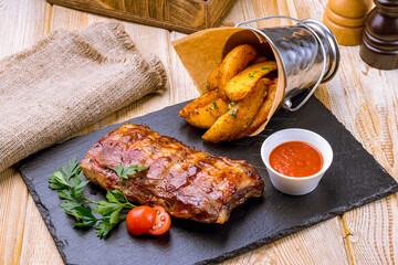 Barbecue pork ribs with fried potato wedges on black stone