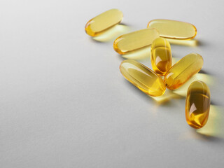 Fish oil. Yellow softgels lie on a white or light gray surface. Vitamins and a healthy lifestyle. Background or backdrop. Copy space for text on the left. Softgel close-up. Omega-3 fatty acids. Macro