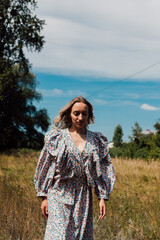  A young woman in a rustic dress walks leisurely through a field in the village