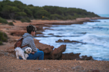 mujer atractiva con perro bichon maltes blanco paseando y contemplando la playa en el mar de oropesa