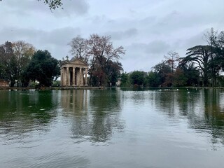 Fototapeta na wymiar Aesthetic photo of a lake with ducks and a Roman temple that is reflected in the water. Villa Borghese