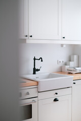 The interior of a kitchen in white tones with a sink, sandwich maker, stove, oven, dining table and a light window