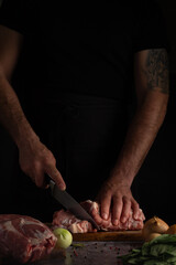A chef in dark attire expertly slices meat on a wooden board, with vegetables and spices nearby.