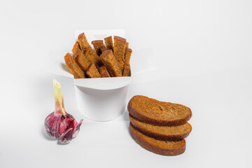 Rusks of black bread lie in a white box near the croutons and garlic on a white background