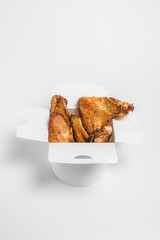 fried chicken wings in oil and breadcrumbs lie in a white box on a white background, top view