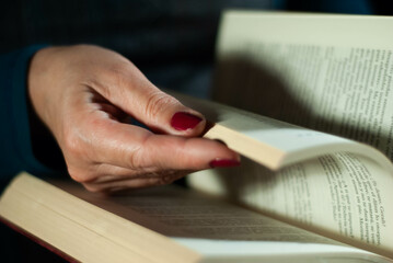 Hands holding a book that an elderly woman is reading using her fingers on the lines filled with words