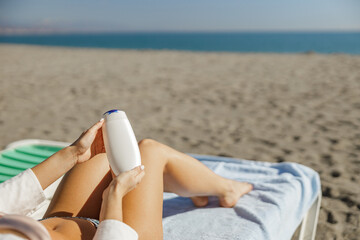 Hands of woman holding sunscreen body lotion while lying on deck chair