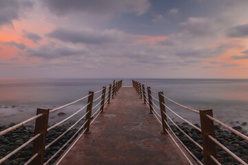 Fototapeta na wymiar Jetty at pebbles beach near Canico at Portugese Madeira Island at sunset time. October 2021. Long exposure picture