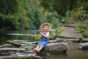 Funny happy little kid fishing at the lake. A fisher boy sits in the lake with a fishing rod and catches fish