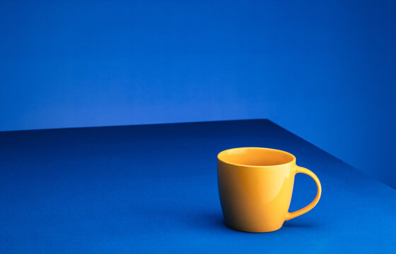 Yellow coffee cup stands on a blue table against a blue background. The concept of minimalism. Place for text
