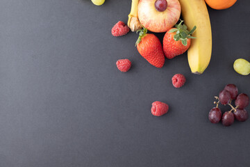 fruit still life on a greyish black background strawberries, apples, bananas, grapes, tangerines with negative space or air for text