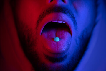Close up of man mouth swallowing ecstasy drugs. Man taking MDMA ecstasy pill. - obrazy, fototapety, plakaty