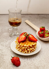 Waffles served with strawberries on a white cutting board on a gray table and a basket with ripe strawberries