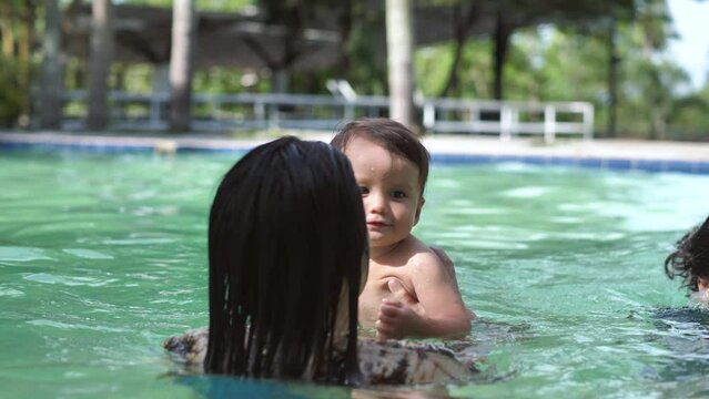 Mom and baby are having fun in the pool, the baby is in waterproof diapers. Water has a good effect on the development of the child's skeleton and nervous system. The kid enjoys dipping into the water