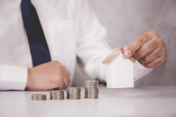 Hands of business man holding  model home and stack of coins, wealth with finance and saving for residence and success, loan and mortgage for residential, investment for real estate, property concept.