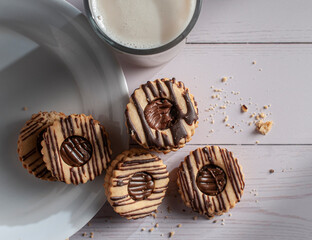 Vanilla cookies stuffed with cream chocolate on a white plate over a white wooden table and a glass of ice milk on the side, horizontal top view overhead or flat lay shot
