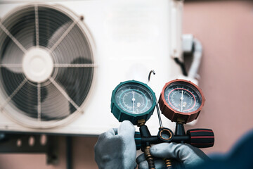 Mechanic air conditioner technician using manifold gauge checking refrigerant for filling home air conditioning and air duct cleaning and maintenance outdoor compressor unit.