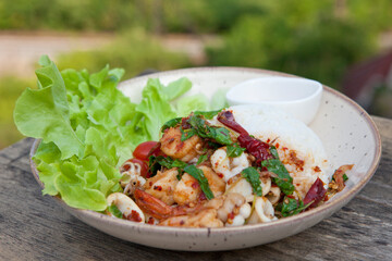 Thai Food - rice topped with Stir Fried Shrimp and Holy Basil on a wooden table.