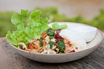 Thai Food - rice topped with Stir Fried Shrimp and Holy Basil on a wooden table.