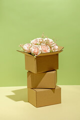 Cardboard boxes packing on and blooming bouquet of pink roses. Gift service and delivery logistics concept.