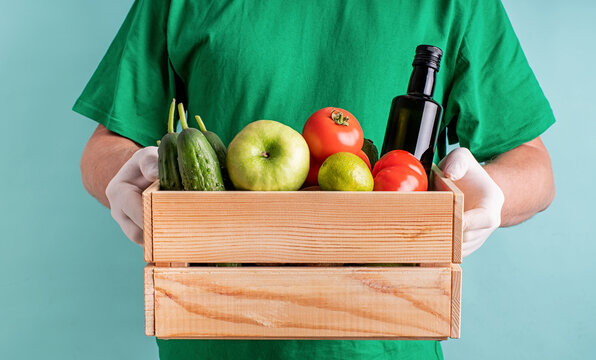 Man in gloves holding a wooden box full of vegetables