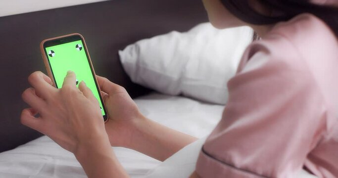 Woman In Pink Pajamas Is Lying On A White Bed, Holding A Phone With A Green Screen With Markers, Makes Two A Two-finger Zoom Gesture. Chroma Key