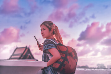 Asian woman traveler taking a photo with temple sunset and pink blue dramatic sky in the...