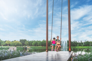 Two asian siblings is swinging on a giant swing in a public park with blue sky.