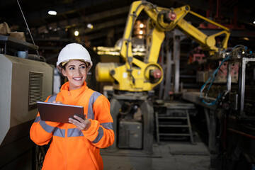 Female engineer using tablet checking and controlling automation robot arms machine in intelligent factory. Welding robotics and manufacturing operation.