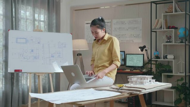 Asian Woman Engineer Sitting On The Table And Using A Laptop To Work At The Office
