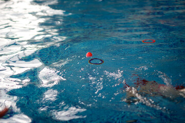 Girl child in a pink swimming cap dives for rings and balls in the pool